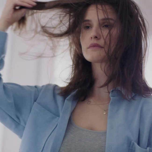 Woman wearing blue shirt is holding up her brown hair