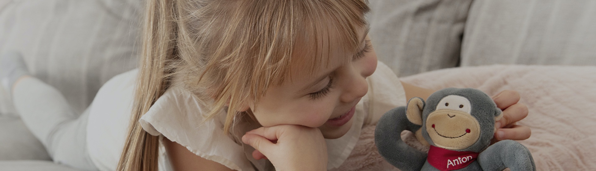 Blonde girl is playing with stuffed animal Anton on the sofa