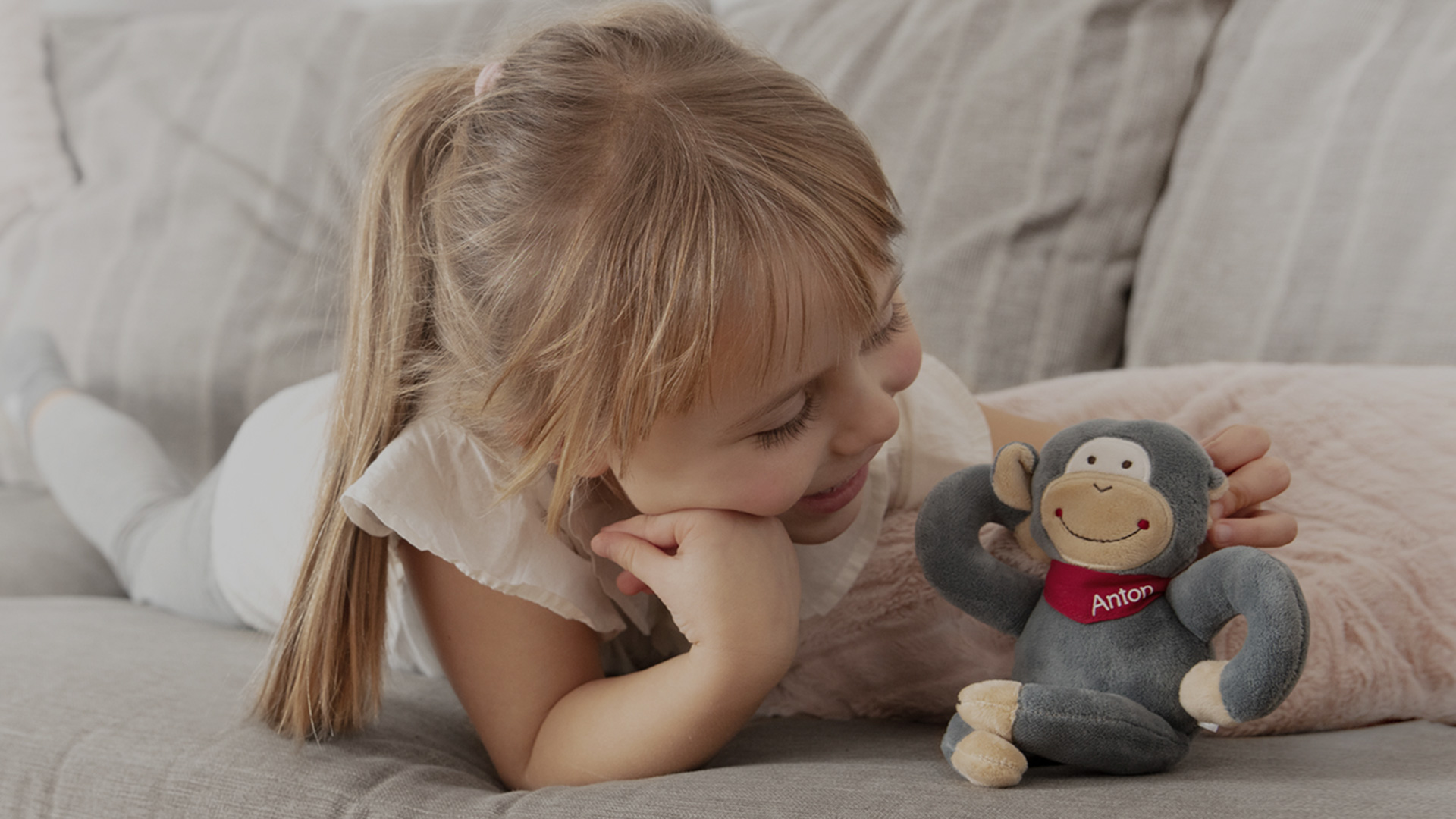 Blonde girl is playing with stuffed animal Anton on the sofa