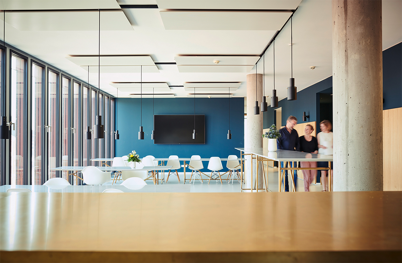 Room with white tables and chairs, on the right side three people are walking through the picture