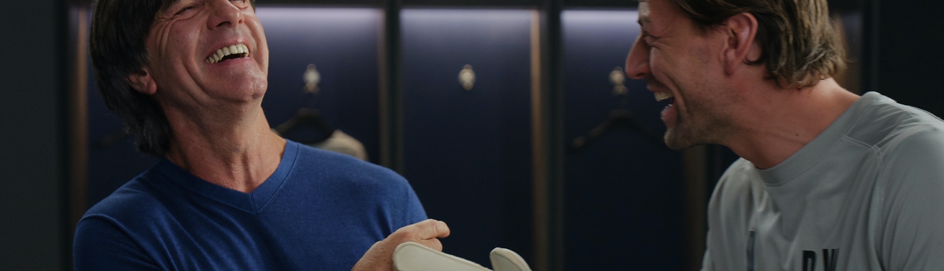 Coach and soccer player inside the changing room, both look at each other and are laughing